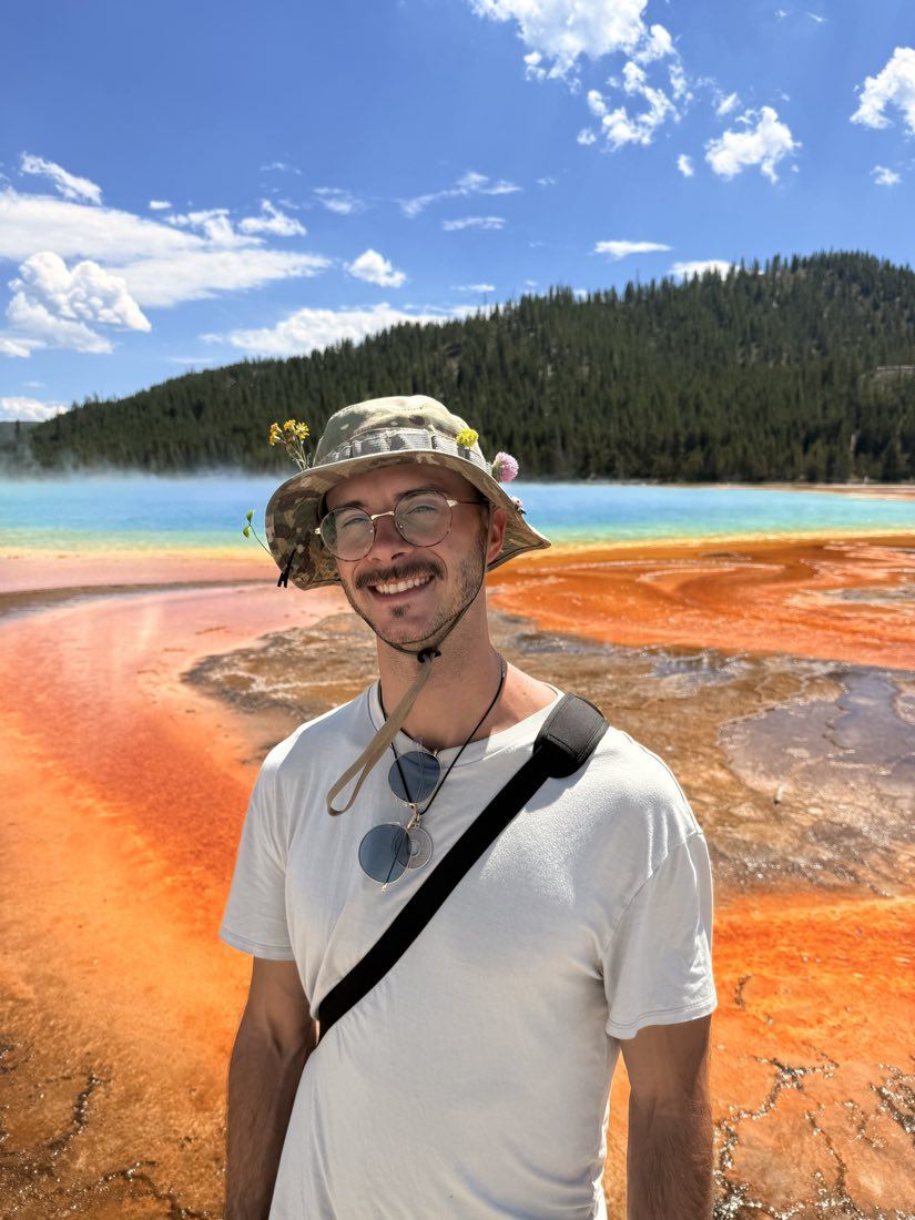 James Thompson smiling in a camouflage boonie hat decorated with wildflowers